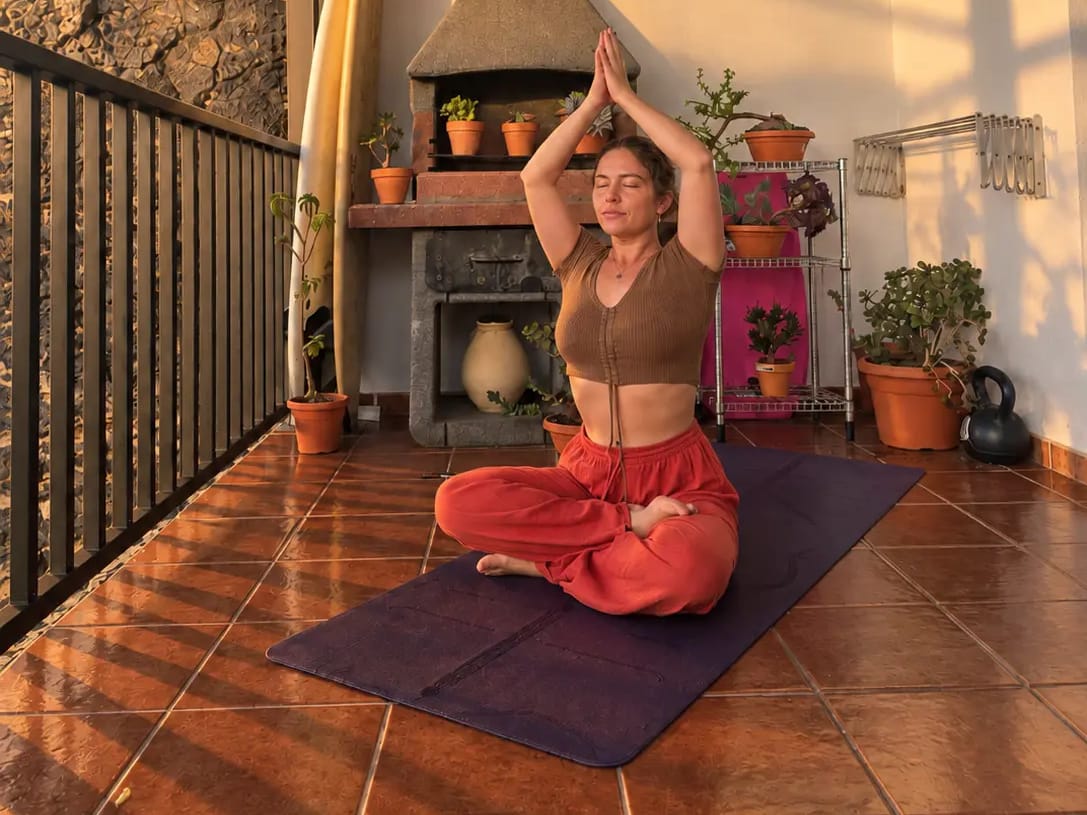 Dani seated cross-legged on a purple yoga mat on her covered terrace at sunset